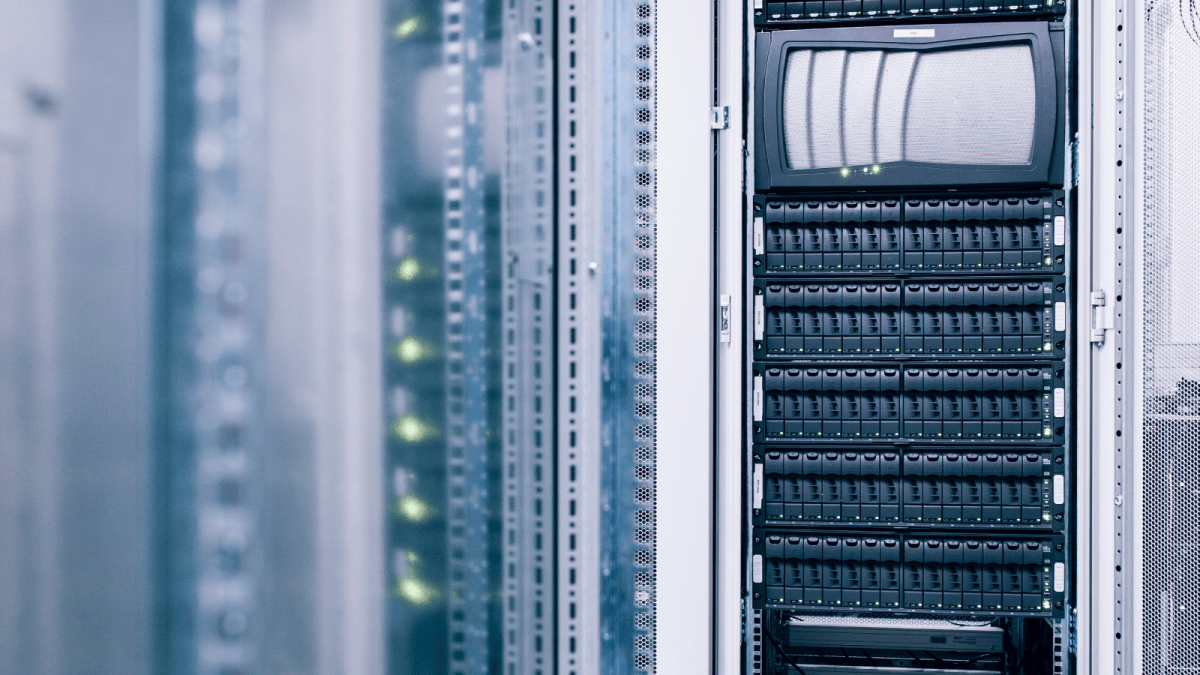 A close-up view of server racks in a data center, with multiple black server units stacked vertically and a monitor screen in one of the racks. Green indicator lights are visible on neighboring equipment featuring Standex Detect technology. by Standex Detect