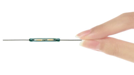 A close-up of a hand gently holding a thin medical device with a cylindrical component in the middle, possibly utilizing Standex Detect Reed Sensors, positioned between two fingers against a white background. by Standex Detect