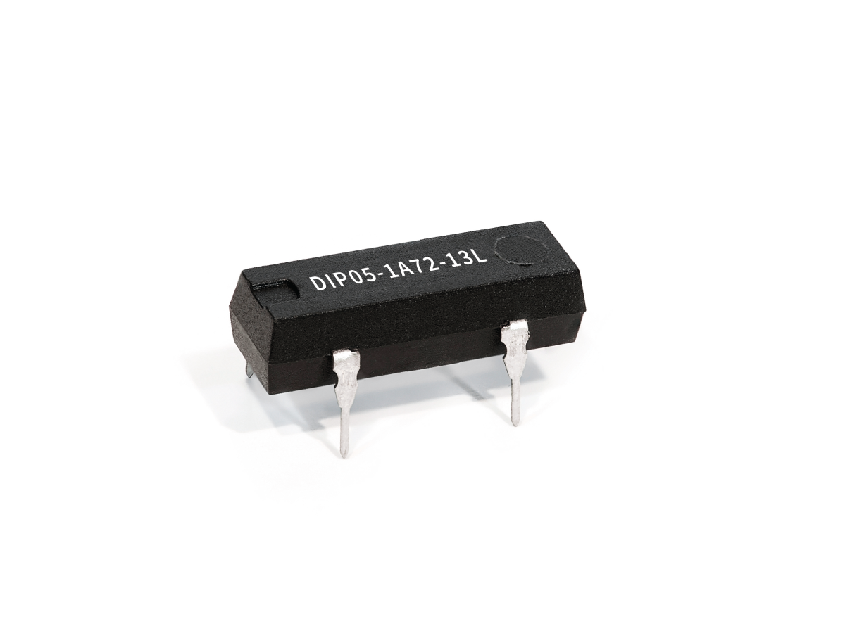A black integrated circuit chip from the DIP Series Reed Relay family, labeled DIP05-1A72-13L, features four metal pins and is placed on a white background. by Standex Detect
