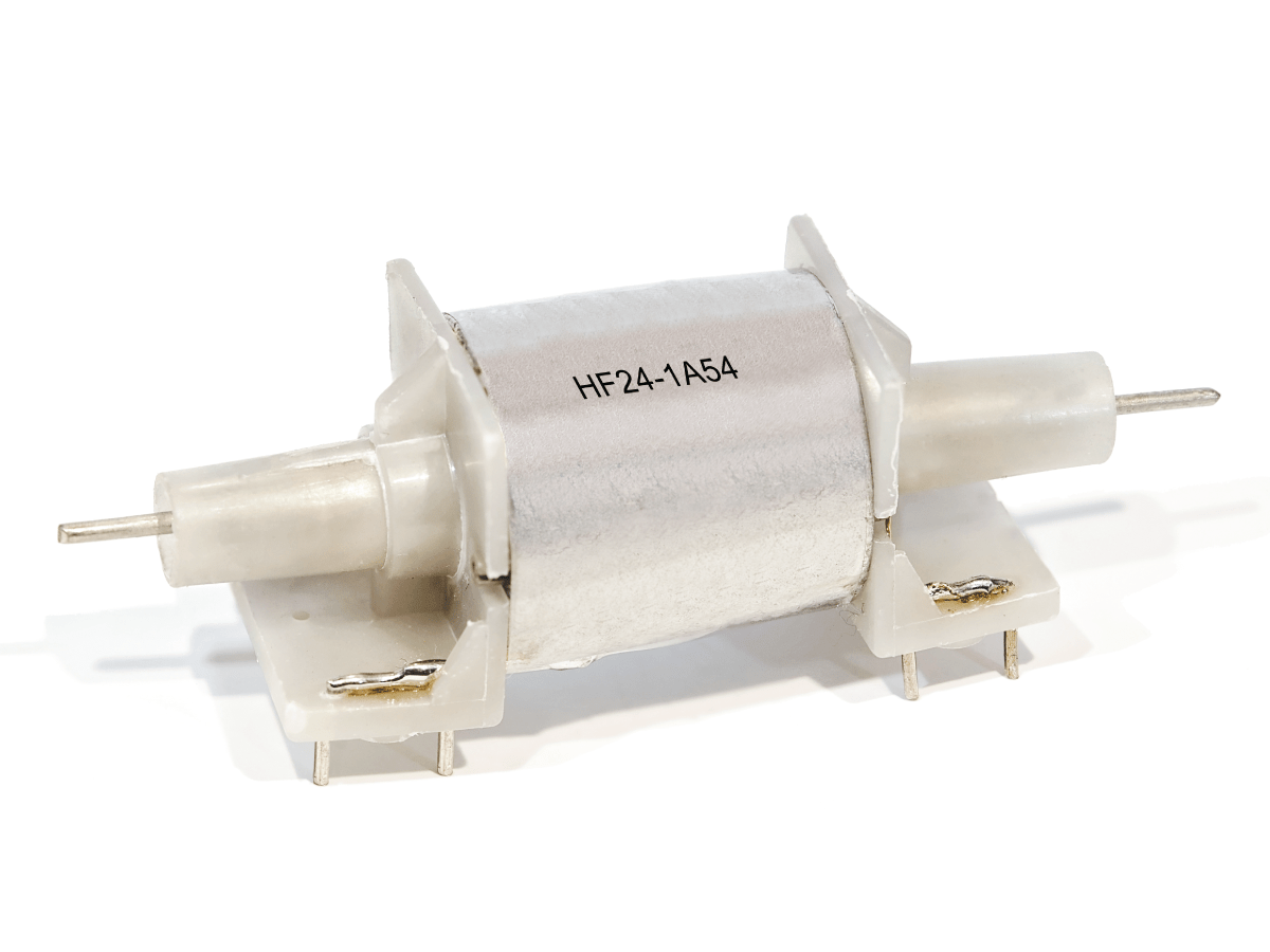A cylindrical Reed Relay with metal pins on both ends, mounted on a white plastic base. The label HF24-1A54 identifies it as part of the HF Series. by Standex Detect