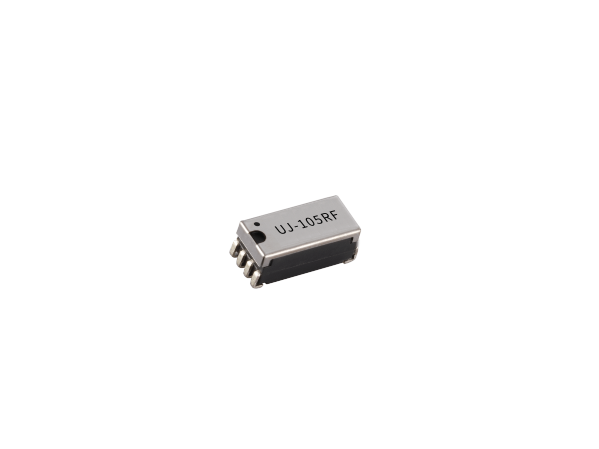 Small black and silver electronic component with metal pins on each side, labeled UJ-105RF, from the U Series Reed Relay lineup, isolated on a white background. by Standex Detect