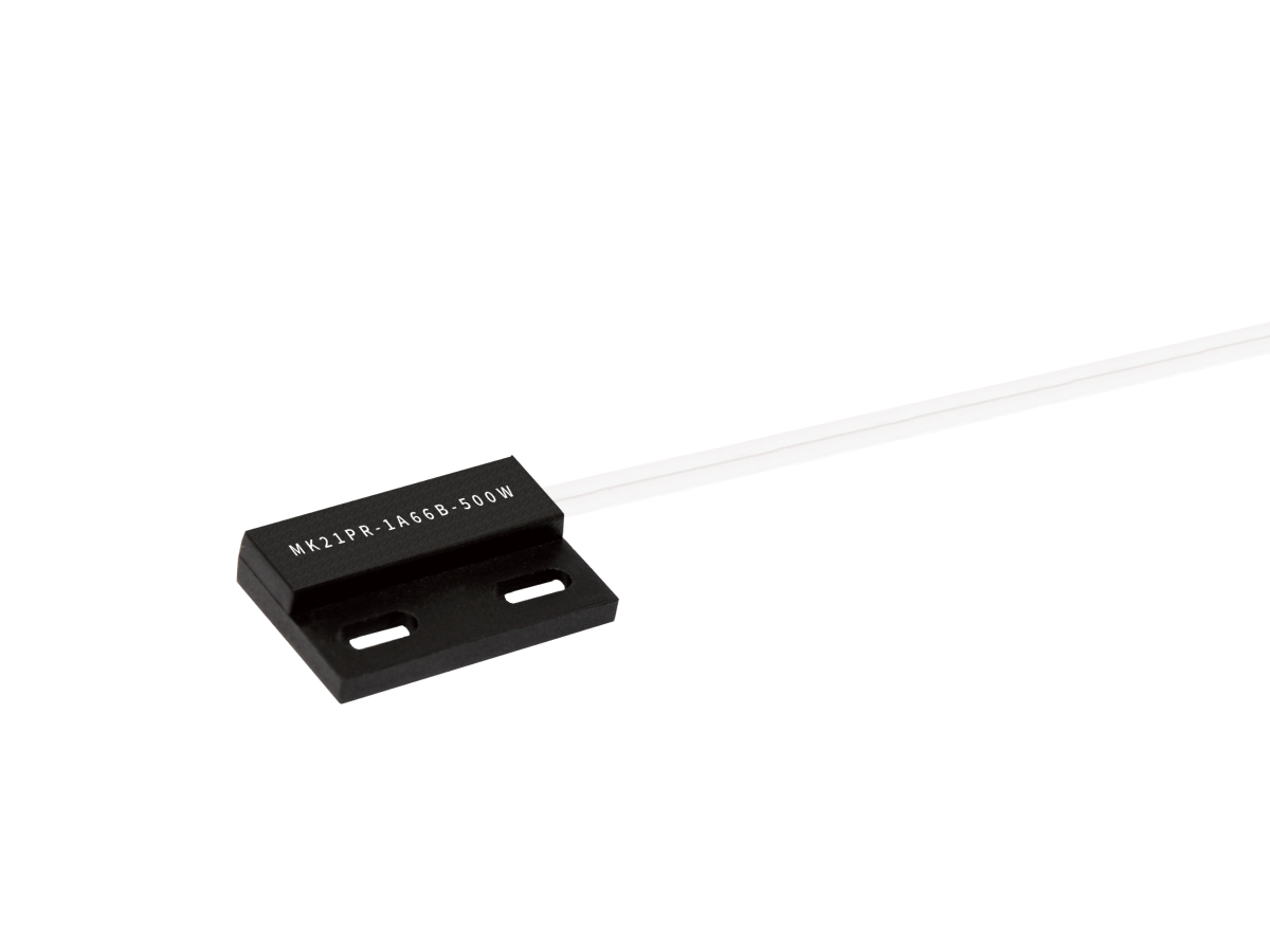 A black rectangular MK21PR Series reed sensor with two mounting holes and a white cable attached on the right side. The sensor has white text printed on its surface, and the background is plain white. by Standex Detect